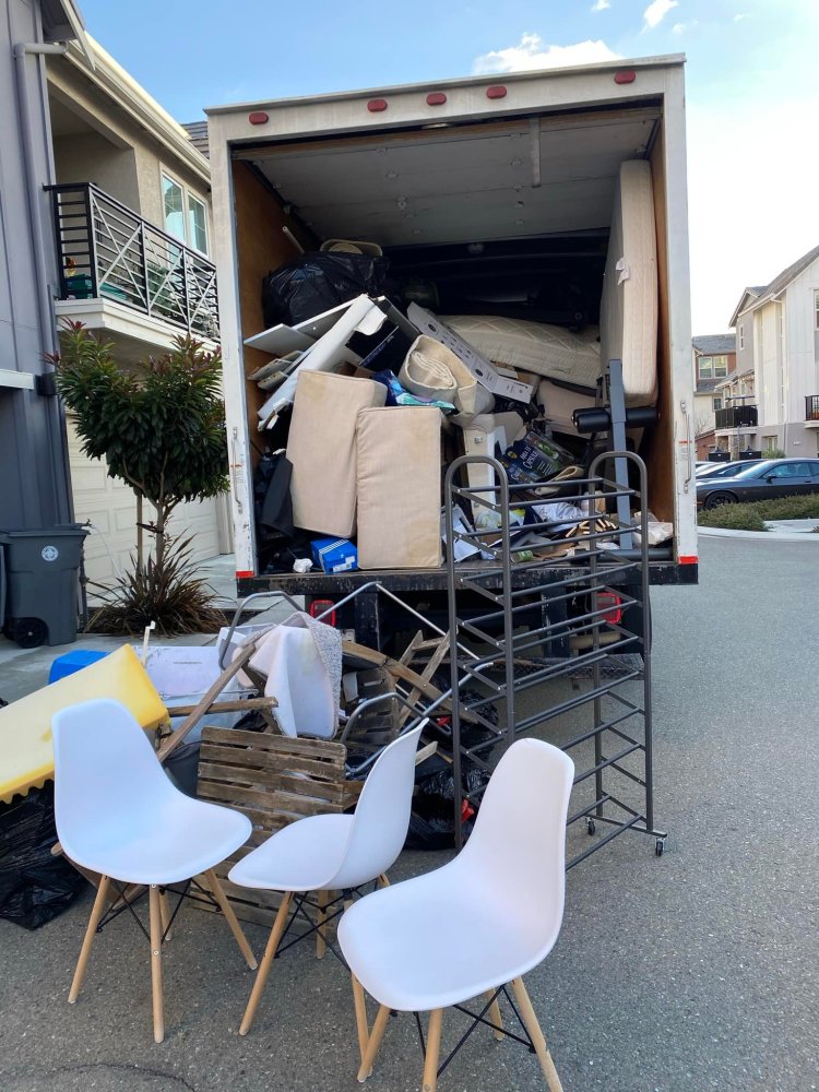 The open back of a moving truck is filled with discarded furniture and household items.